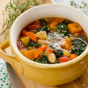 Autumn Vegetable Soup in a yellow bowl on cutting board with herbs in the background
