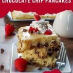 3 baked chocolate chip pancakes piled on a plate with strawberries and whipped cream.