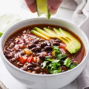 canned black bean soup in a white bowl with lime being squeezed from top