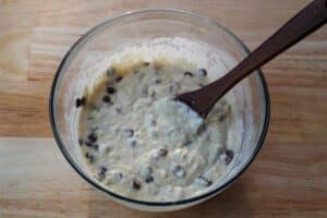 milk chocolate chips added to mixture in glass bowl with wooden spoon