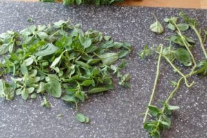 oregano leaves being removed from stems on grey cutting board
