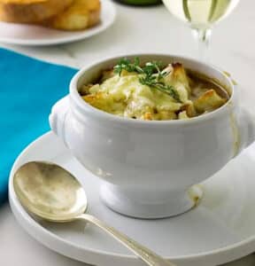 French Onion Soup in a white bowl on white plate, with spoon