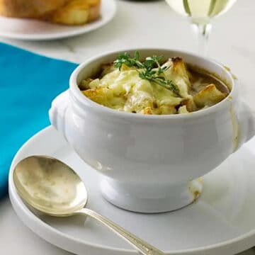 French Onion Soup in a white bowl on white plate, with spoon