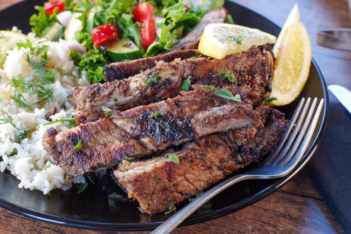 Cut Greek ribs on a plate with Greek rice and salad, with fork on plate