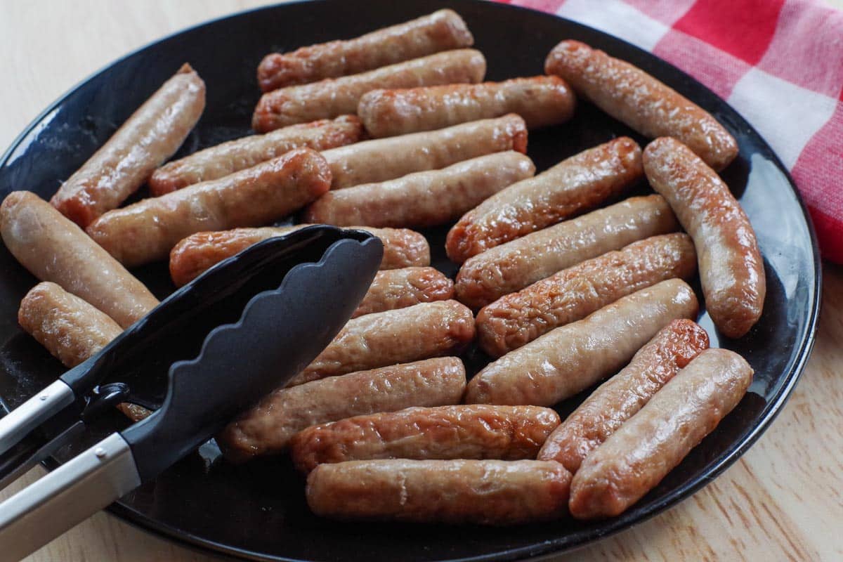 2 packages of air fried turkey sausages on a black plate with tongs on the side