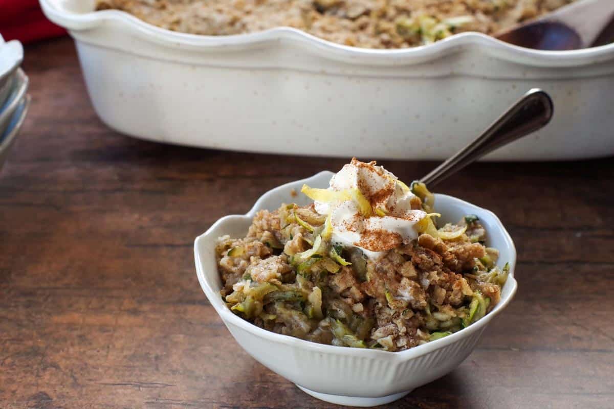 zucchini crisp in a white bowl with a baking dish with more zucchini crisp in background