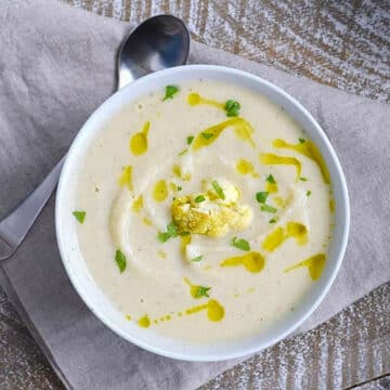roasted cauliflower and garlic soup in a white bowl on grey linen