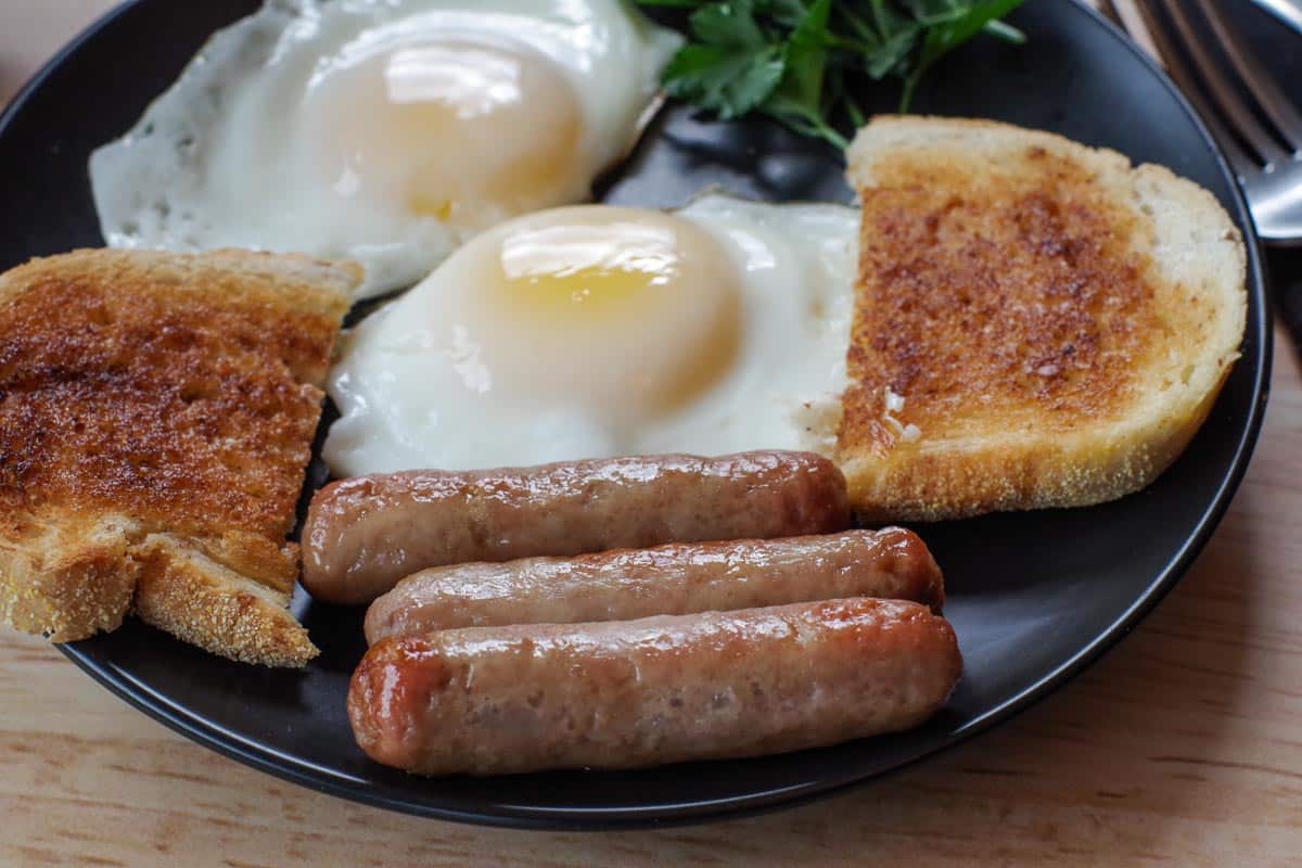 3 air fryer turkey sausages on a black plate with eggs and toast and parsley