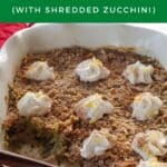 zucchini crisp, dotted with whipped cream, in a white baking dish with some missing and a wooden spoon