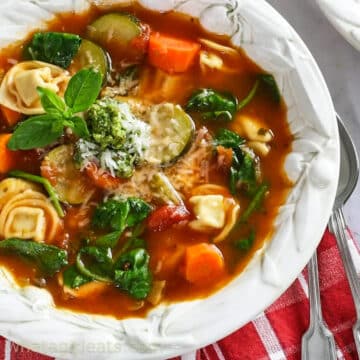 spinach tortellini soup in white bowl with spoon on the side
