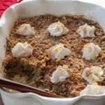 zucchini crisp in large white baking dish, dotted with whipped cream, with wooden spoon and some dessert taken out