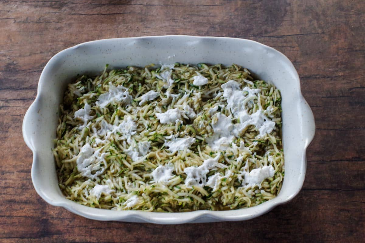 zucchini mixture in white baking dish, dotted with whipped cream