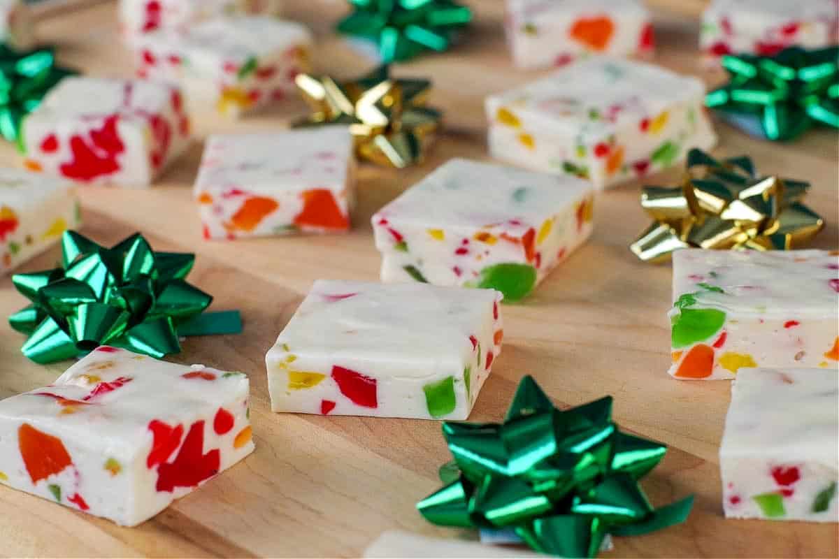 Nougat candy, cut into squares, on a wooden cutting board with green and gold mini bows
