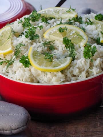 Greek rice with lemon and herb garnish in orange dish