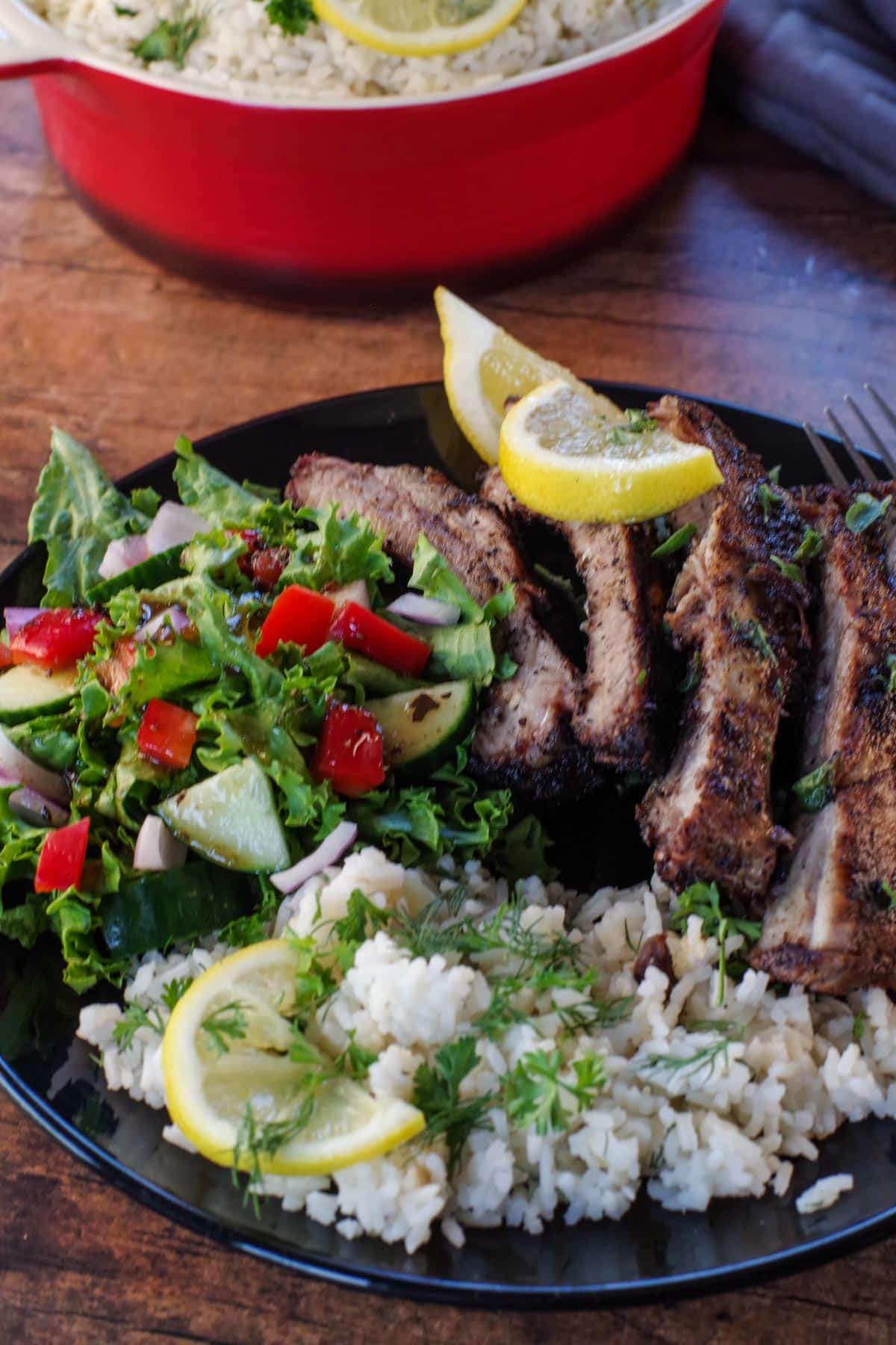 eek rice with Greek ribs and salad on a black plate.