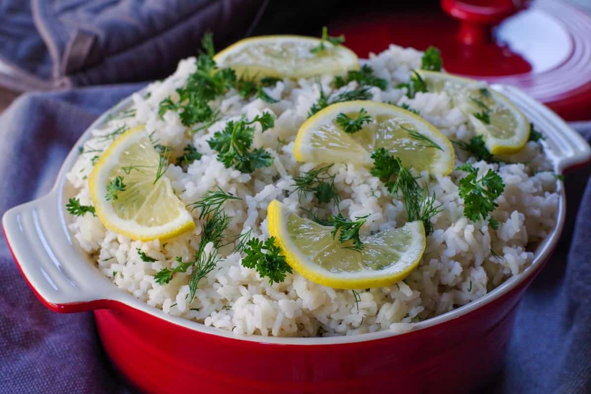 Greek rice with lemon and herb garnish in orange dish
