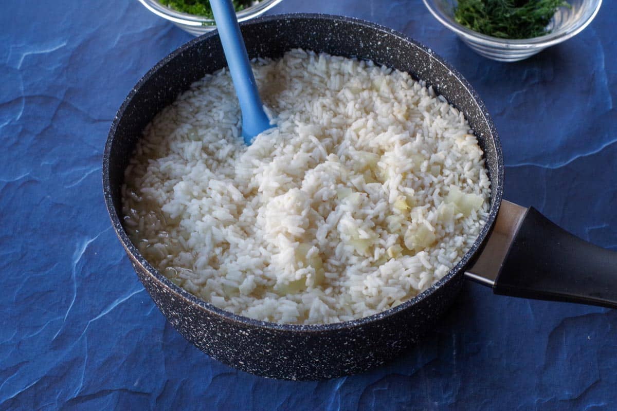 rice with broth, lemon juice, garlic and onion in a black pot