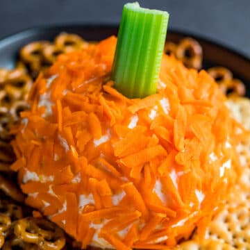 Halloween cheese ball shaped like a pumpkin with celery for a steam and crackers around it