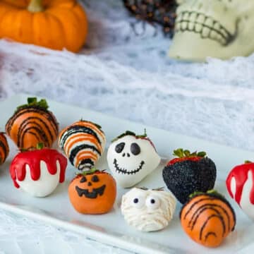 Halloween chocolate covered strawberries on a white long rectangular platter with skull and pumpkin decorations in background