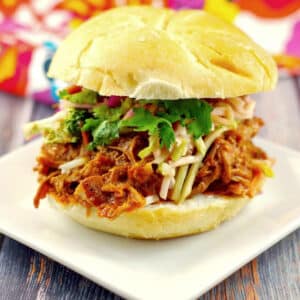 slow cooker pulled pork sandwich on a white plate with a colorful tea towel in the background