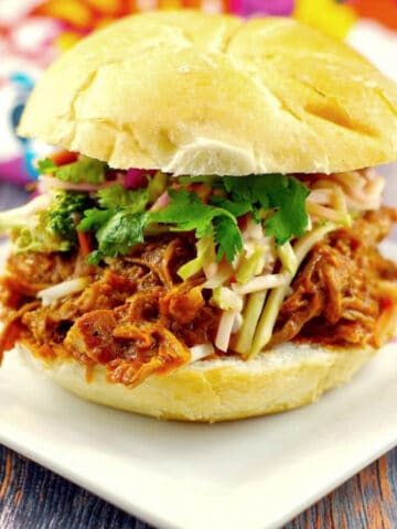 slow cooker pulled pork sandwich on a white plate with a colorful tea towel in the background