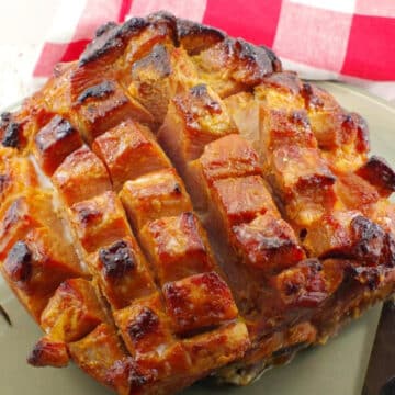 Picnic ham on a platter with a red checkered towel in background