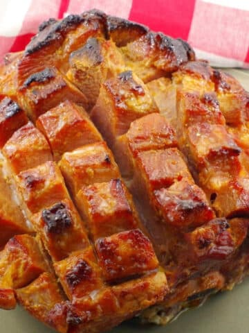 Picnic ham on a platter with a red checkered towel in background