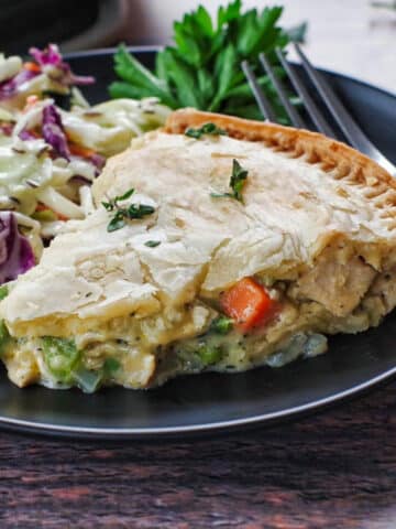 slice of turkey pot pie on a black plate with coleslaw