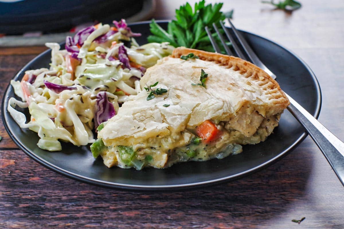 slice of turkey pot pie on a black plate with coleslaw