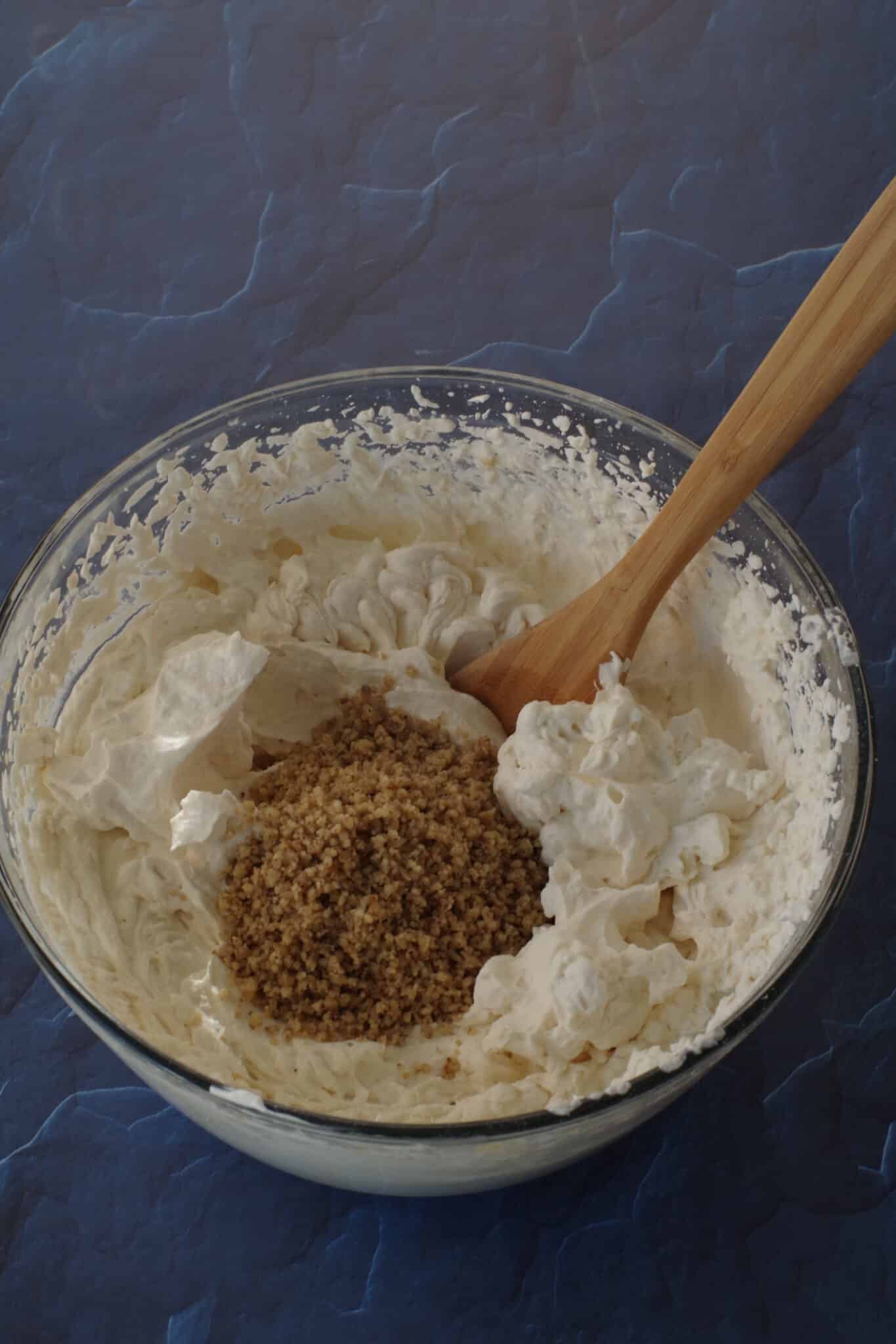 ground walnuts in glass bowl with whipped cream frosting and wooden spoon