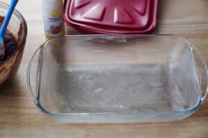 greased glass pan with red lid and bottle of cake release in the background