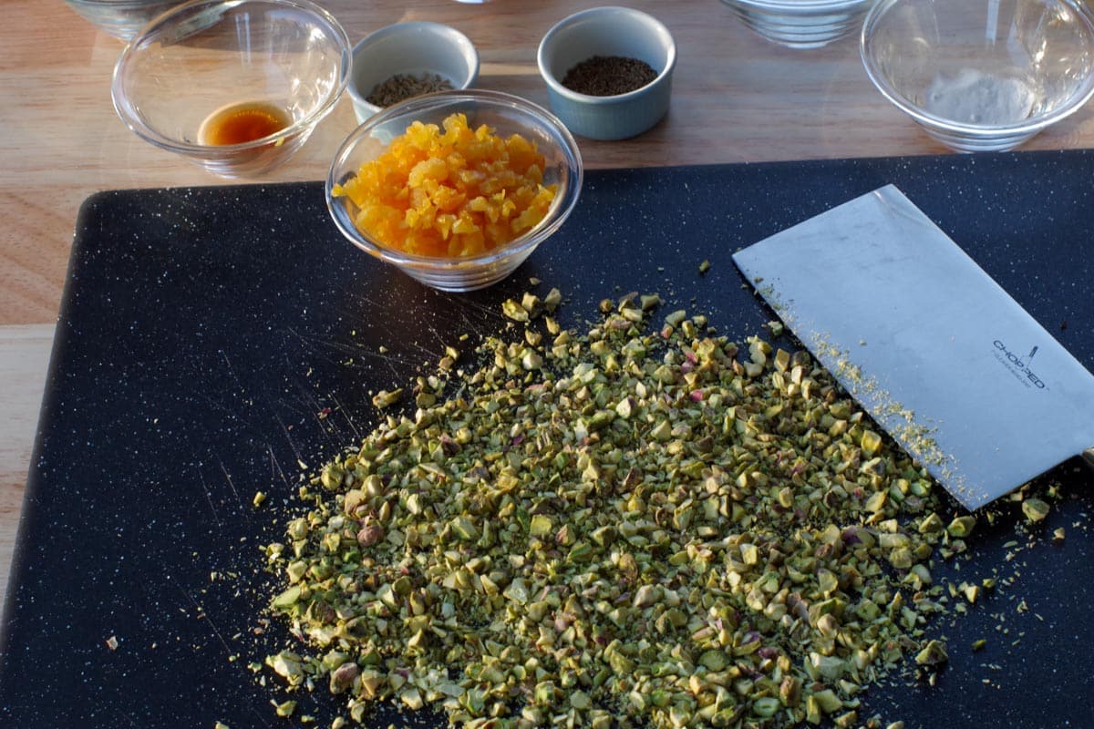pistachios chopped on a cutting board, with knife and apricot and other ingredients in background