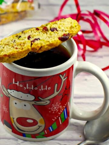 Christmas biscotti sitting on a Christmas mug of coffee with a spoon to the right