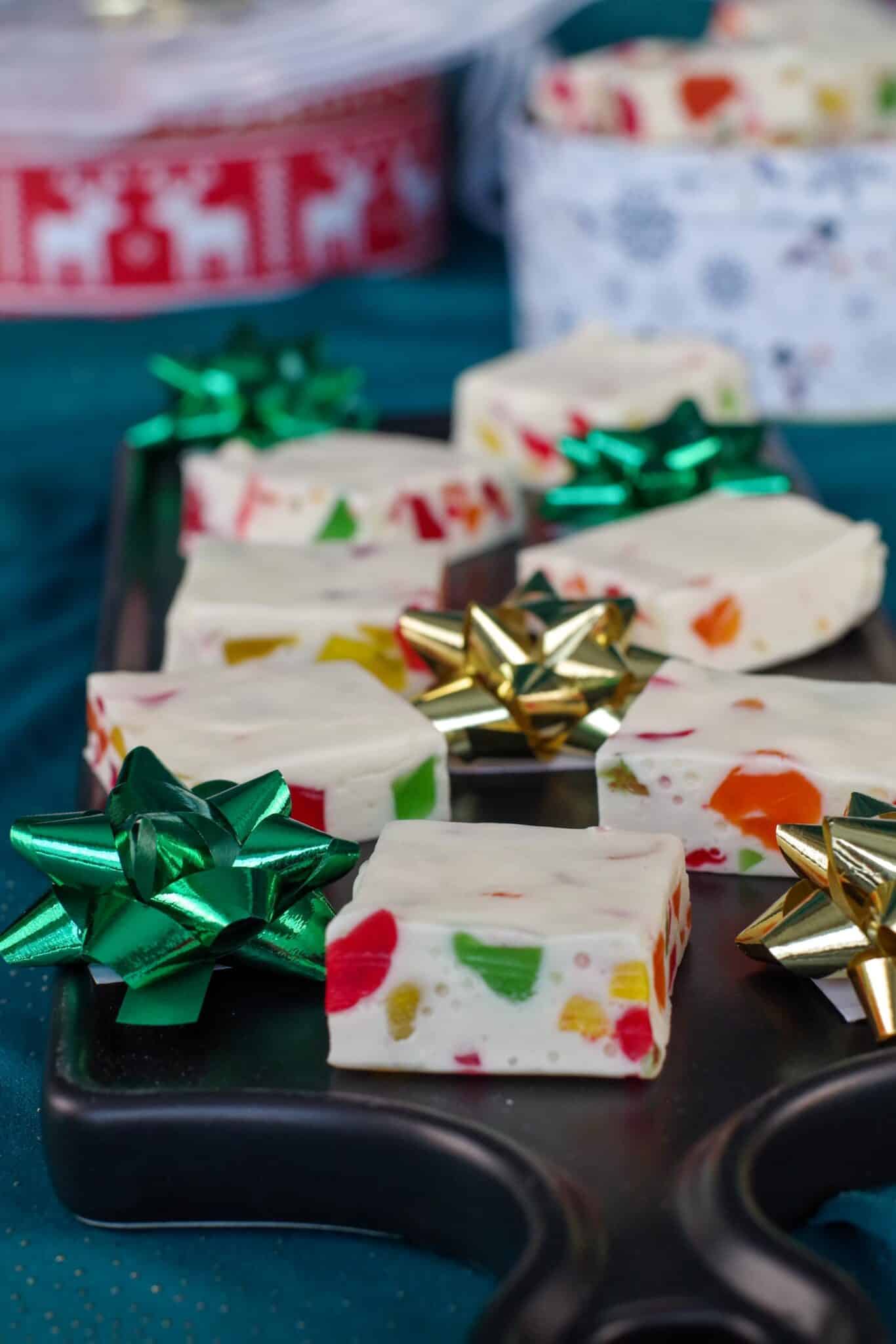 Christmas Nougat Candy on narrow black serving platter with bows and cookie tins in the background