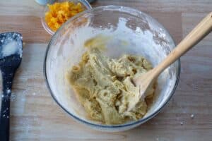 flour mixed into dough mixture with wooden spoon in glass bowl