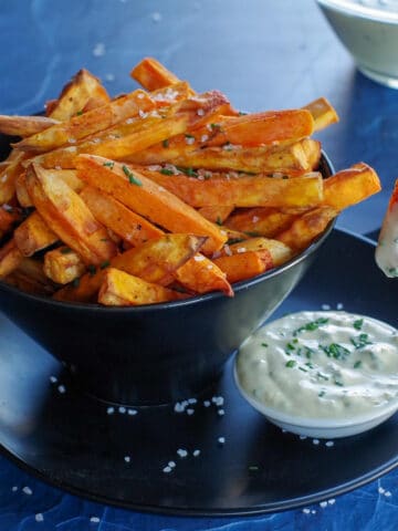 bowl of sweet potato fries and dip, with fry being dipped into white bowl of dip
