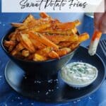 black bowl of sweet potato fries and dip, with fry being dipped into white bowl of dip