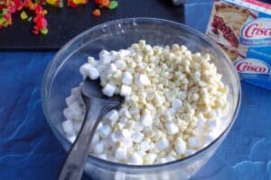 marshmallows, white chocolate chips and butter in a large glass bowl with a black spatula