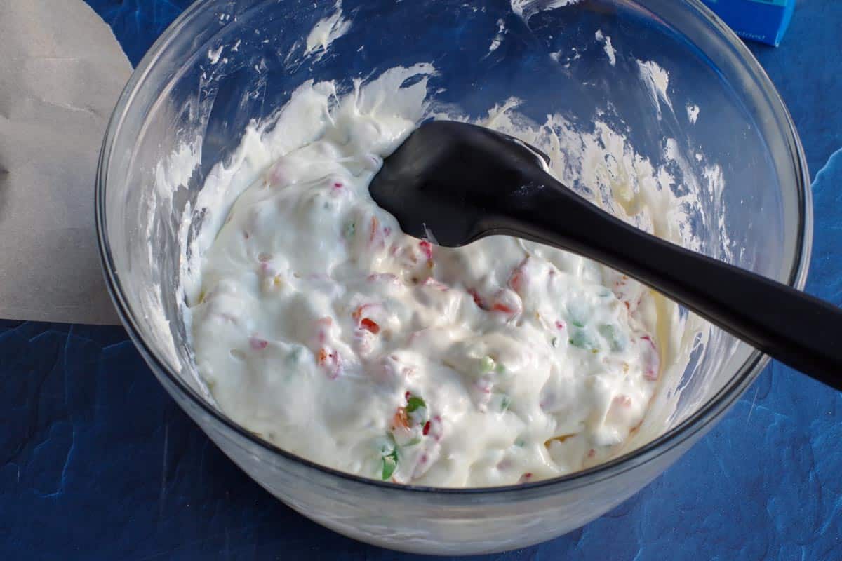 jujubes stirred into marshmallow mixture in a large glass bowl with a black spatula