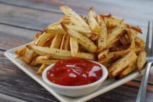 parsnip fries with a white bowl of ketchup on white plate