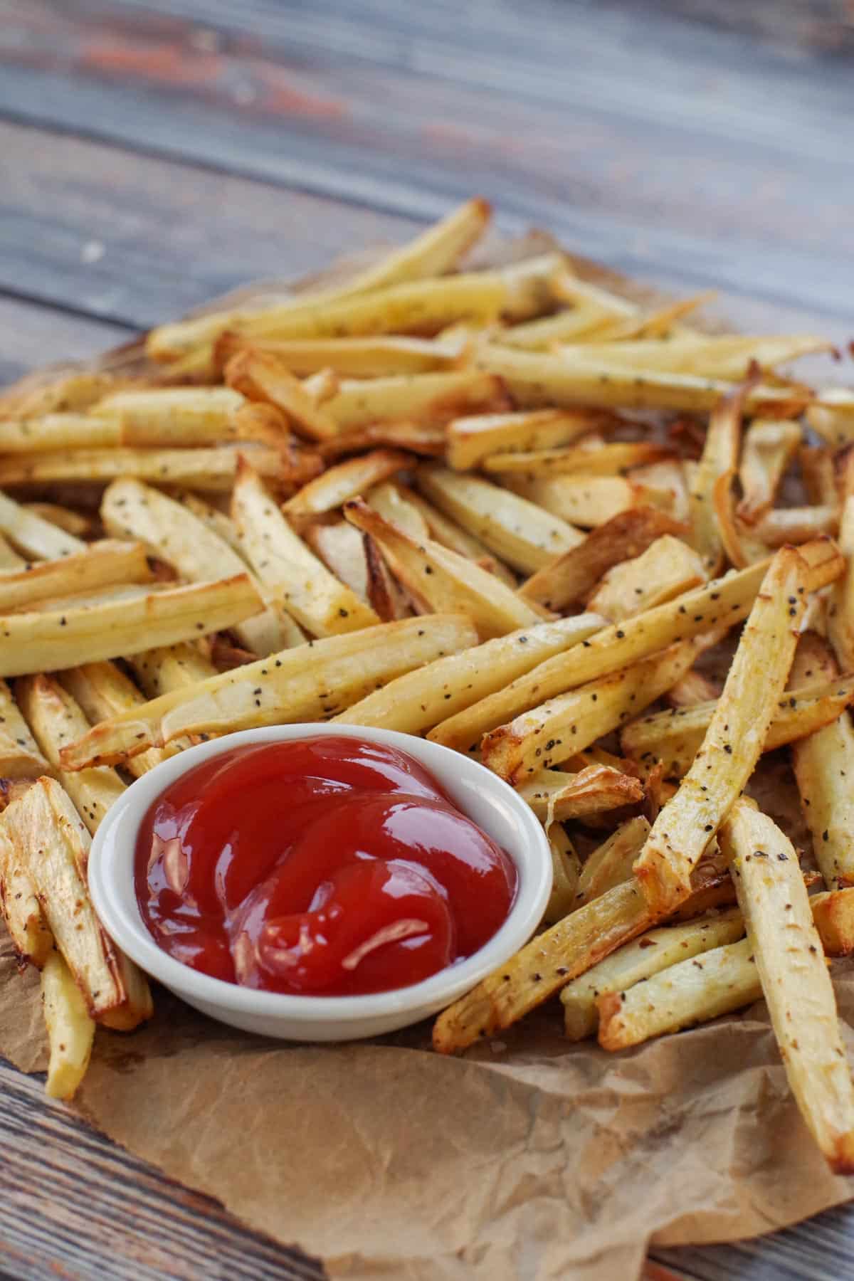 parsnip fries on brown paper with white bowl of ketchup