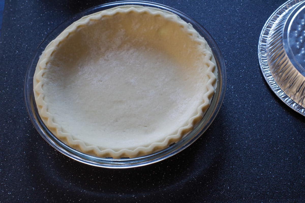 store-bought pie shell in a glass pie plate with aluminum pie plate to the right side