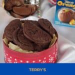 pin with photo of Terry's chocolate orange cookies in a red and white cookies tin with a chocolate orange open and chocolate orange box in the background