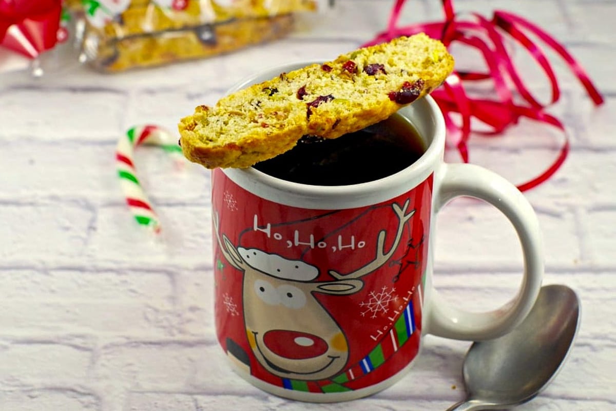 Christmas biscotti sitting on a Christmas mug of coffee with a spoon to the right