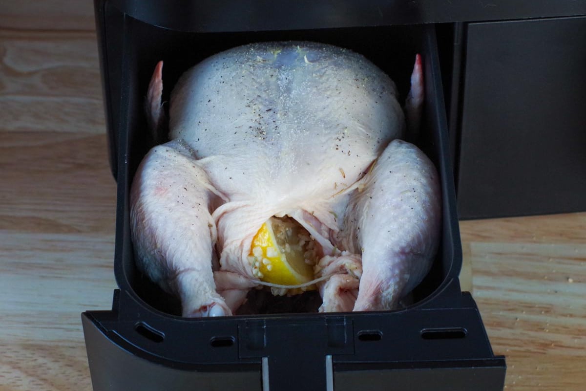 whole chicken in drawer of air fryer with salt and pepper sprinkled on