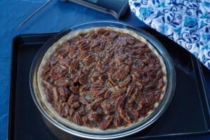 baked pecan pie on black baking sheet with blue patterned oven mitts