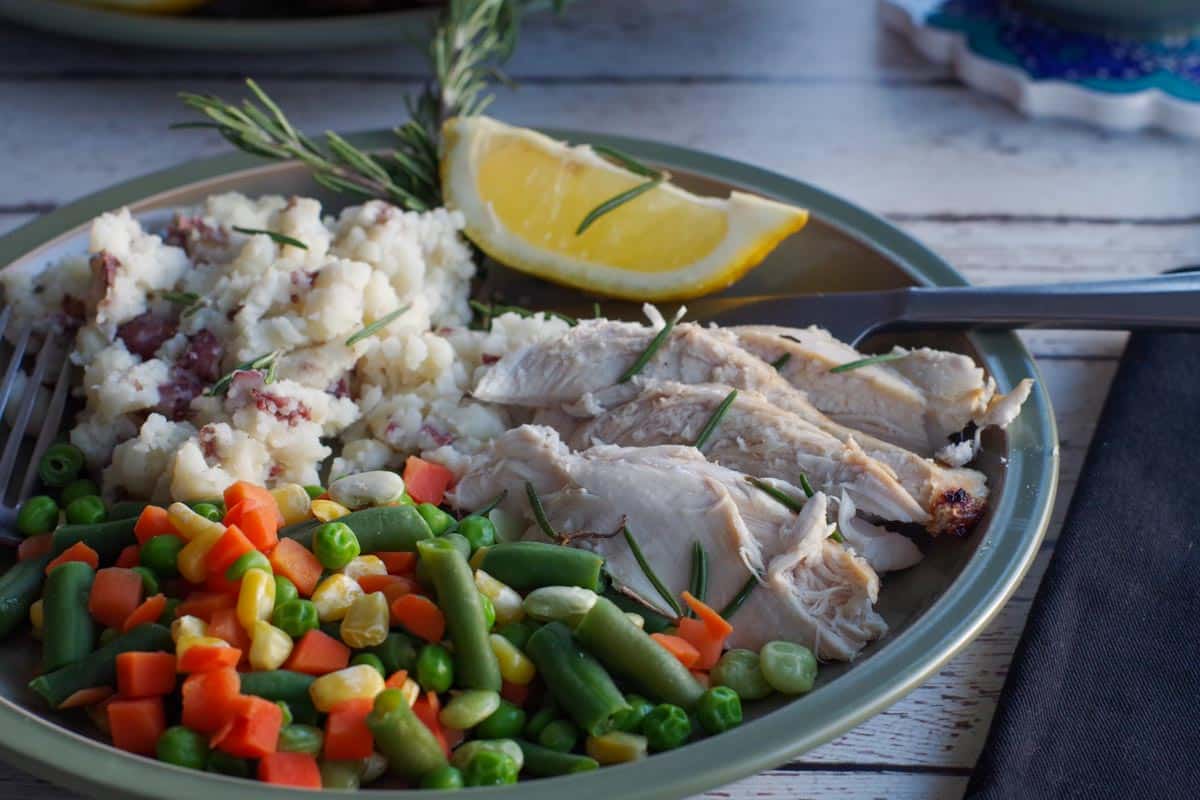 sliced air fyer chicken on a green plate with mixed vegetables, mashed potatoes and mixed vegetables