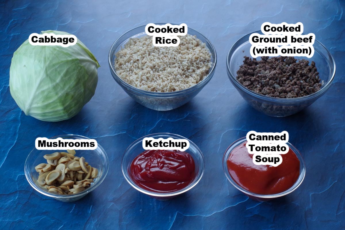 cabbage roll ingredients, labelled in glass bowls, on blue surface