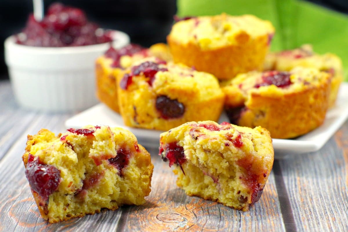 cranberry cornbread muffin spilt in half with a plate of muffins in background