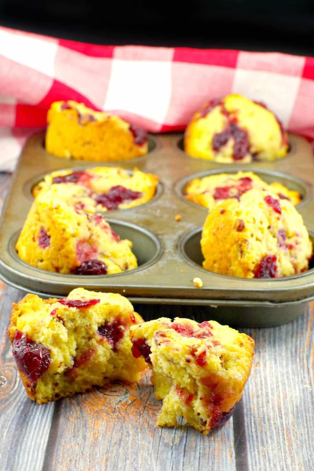 cranberry cornbread muffin spilt in half with a tin of muffins in the background